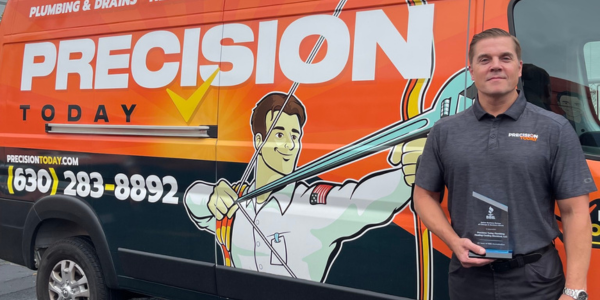 Precision Today team member holding an award beside a branded plumbing and drains service van