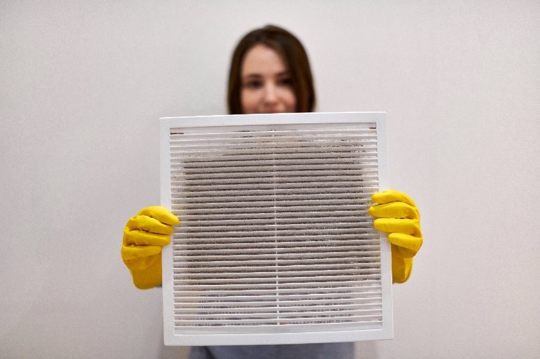 A young woman holding dirty and dusty ventilation grille in her home in Carol Stream, IL.