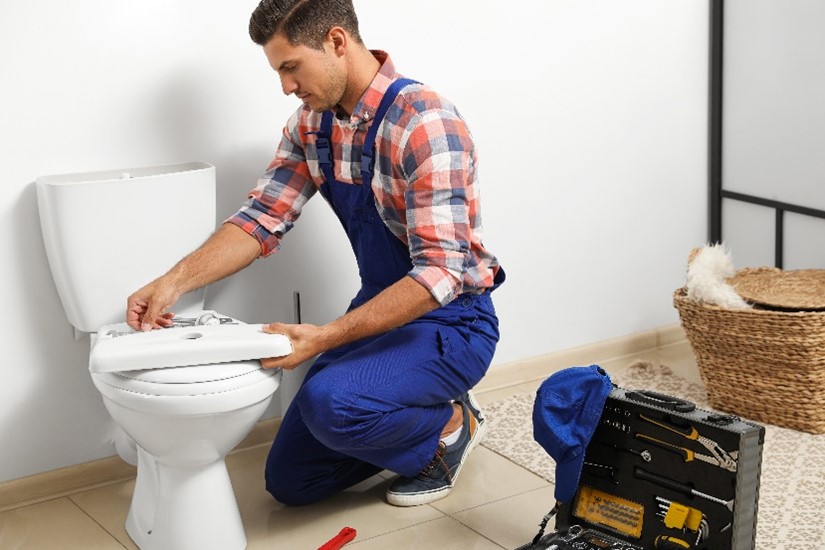 Professional male plumber with toolbox working on repairing a toilet in a bathroom in Carol Stream, IL.