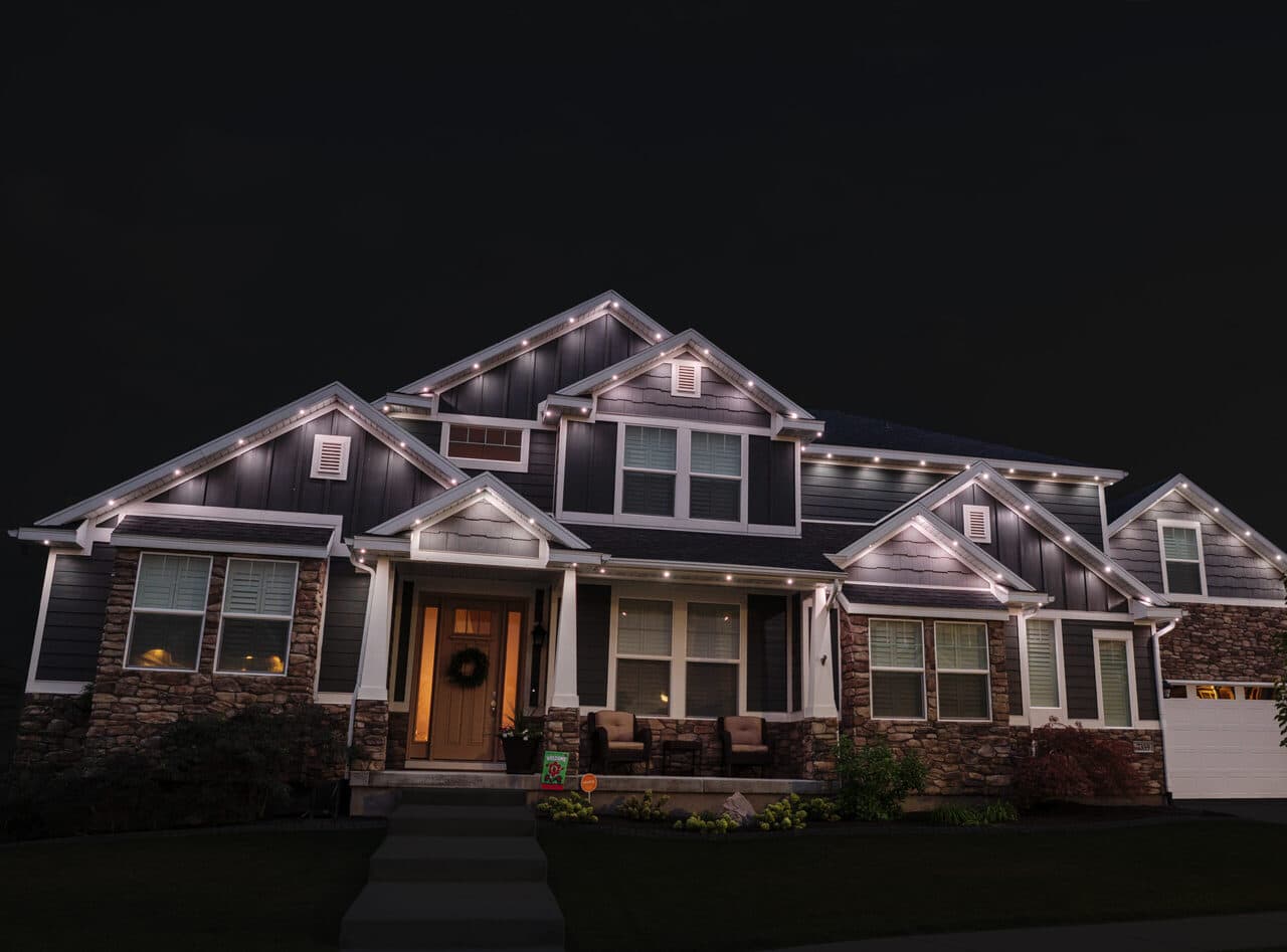 Two-story suburban house with warm interior lights glowing at dusk