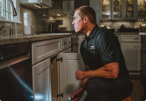 Precision Today plumber kneeling to work under a kitchen sink